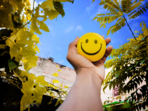 Hand Holding up Yellow Smile Ball in Urban Setting