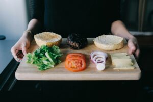 woman holding cutting board with burger and fixings emy 90710FOygrg unsplash copy